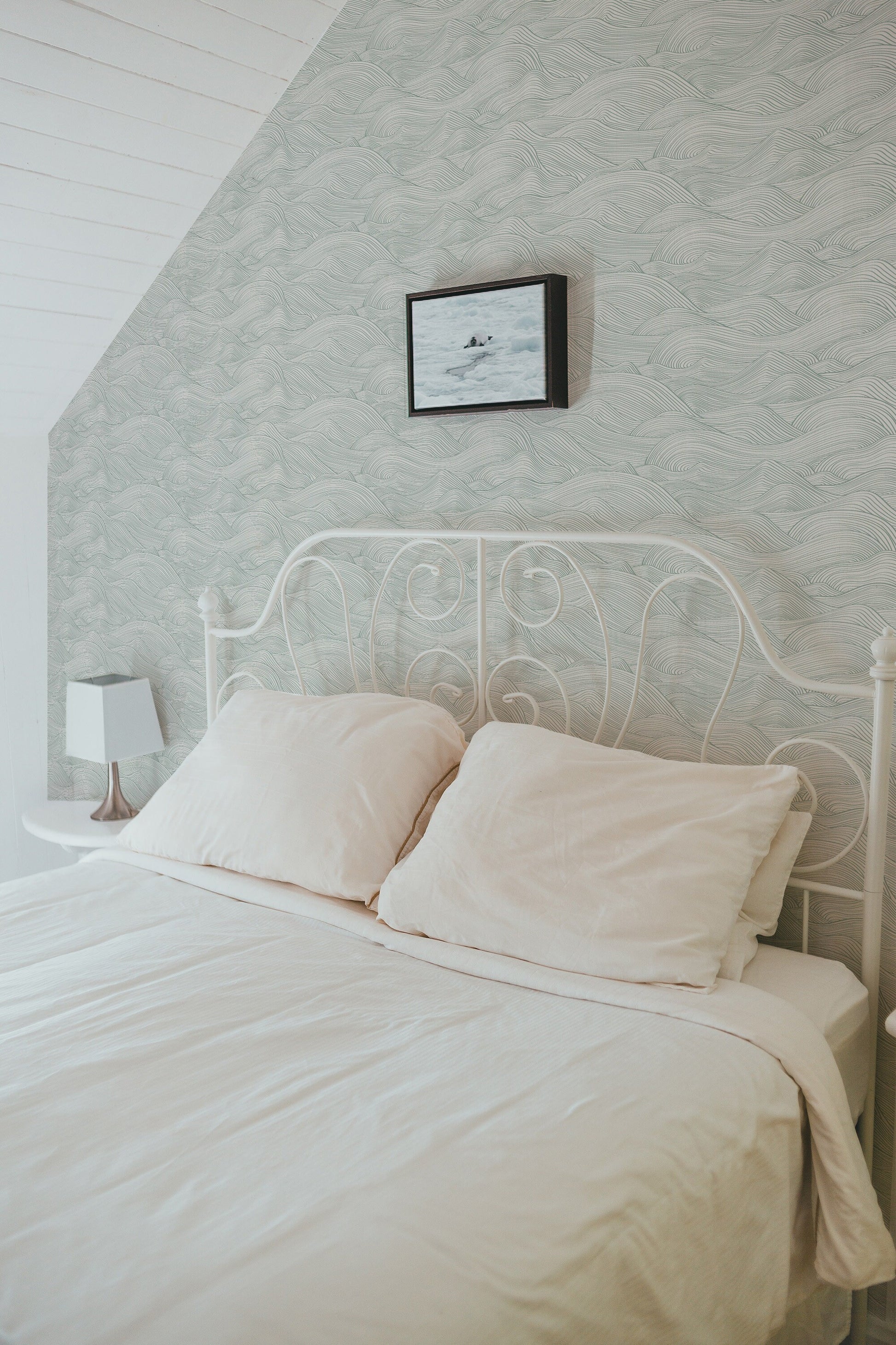 a white bed with two pillows and a picture on the wall